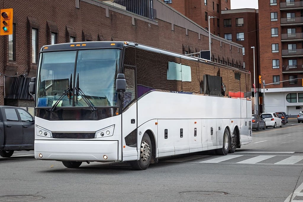 Spacious white coach driving on an Edinburgh road, passing historic buildings.
